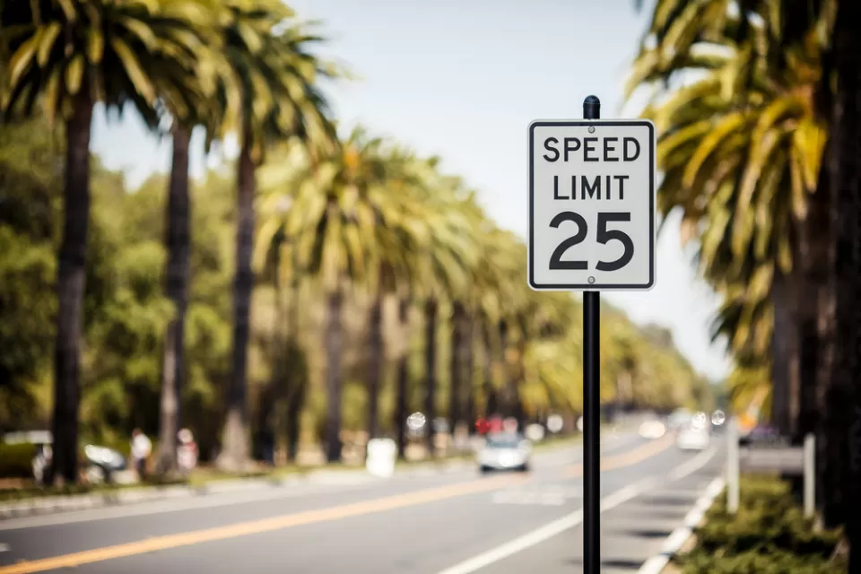25mph speed limit sign with blurred street with car and palm trees in background